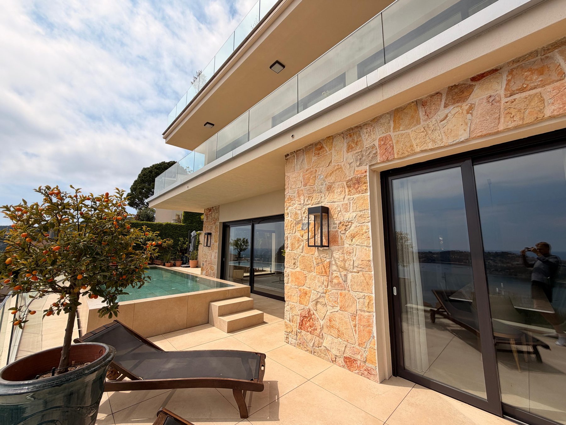 Stone facade, glass and the pool terrace in the afternoon sun